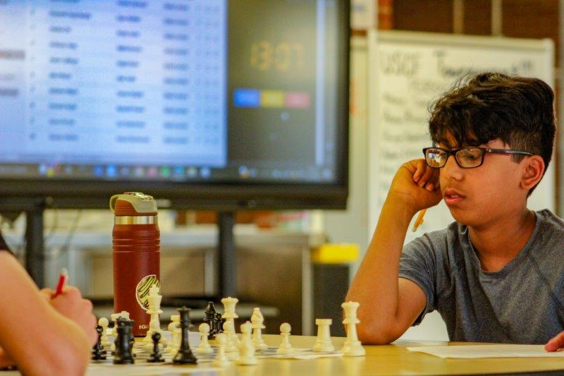 a student is sitting at a table looking at a chess game