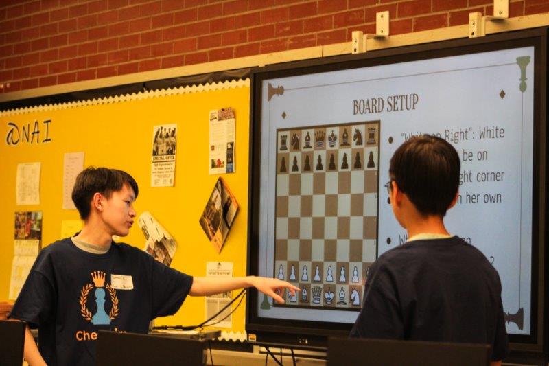 2 students are teaching a chess move on a large screen.